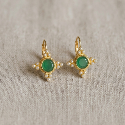 Pair of gold earrings with green gemstones on a textured beige background