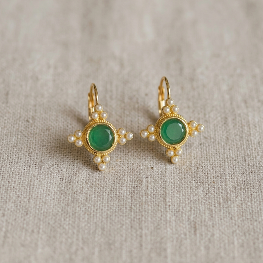 Pair of gold earrings with green gemstones on a textured beige background