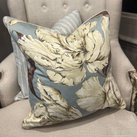 This stunning Peony Floral Cushion in Duck Egg Blue is crafted from a premium cotton blend fabric showcasing an elegant floral design in cream and taupe. Filled with soft feathers, it offers exceptional comfort, complemented by natural self-piping for a refined finish.