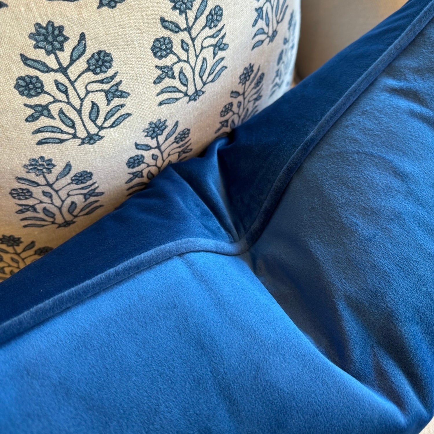 Close-up of a blue cushion and a beige cushion with floral patterns.