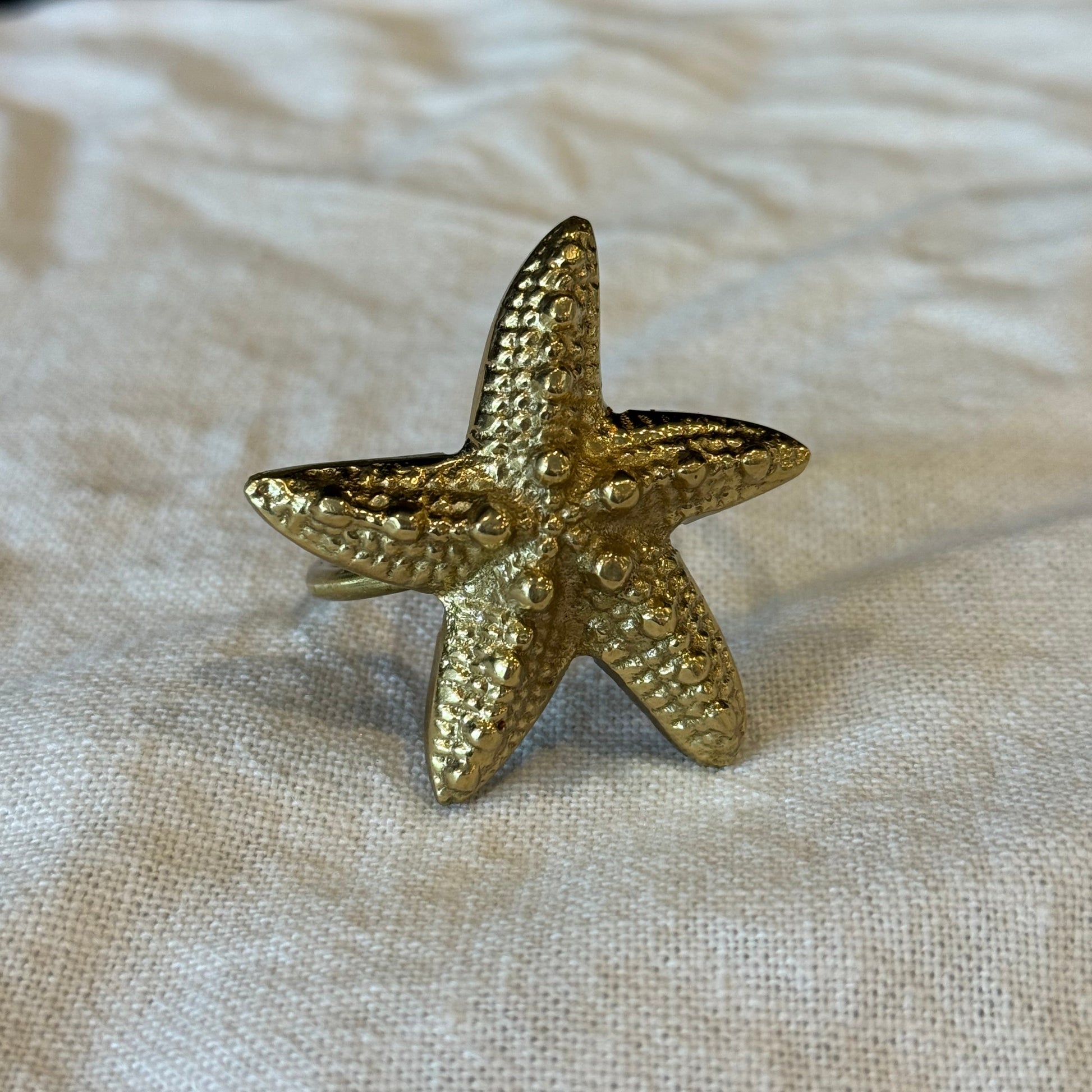 Gold starfish-shaped brooch on a textured beige fabric background