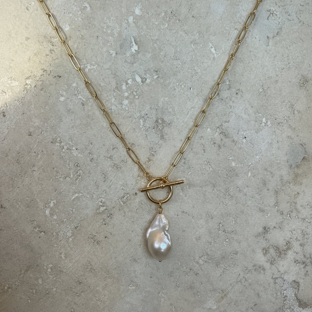 Gold necklace with a pearl pendant on a textured surface