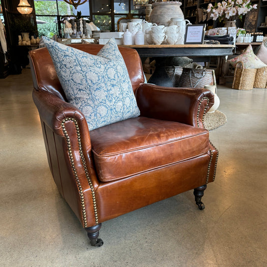 The Oliver Aged Leather Armchair boasts top grain cowhide upholstery, expertly aged by hand for a timeless and vintage appearance. Finished with charming brass stud accents and castor wheel feet. Front