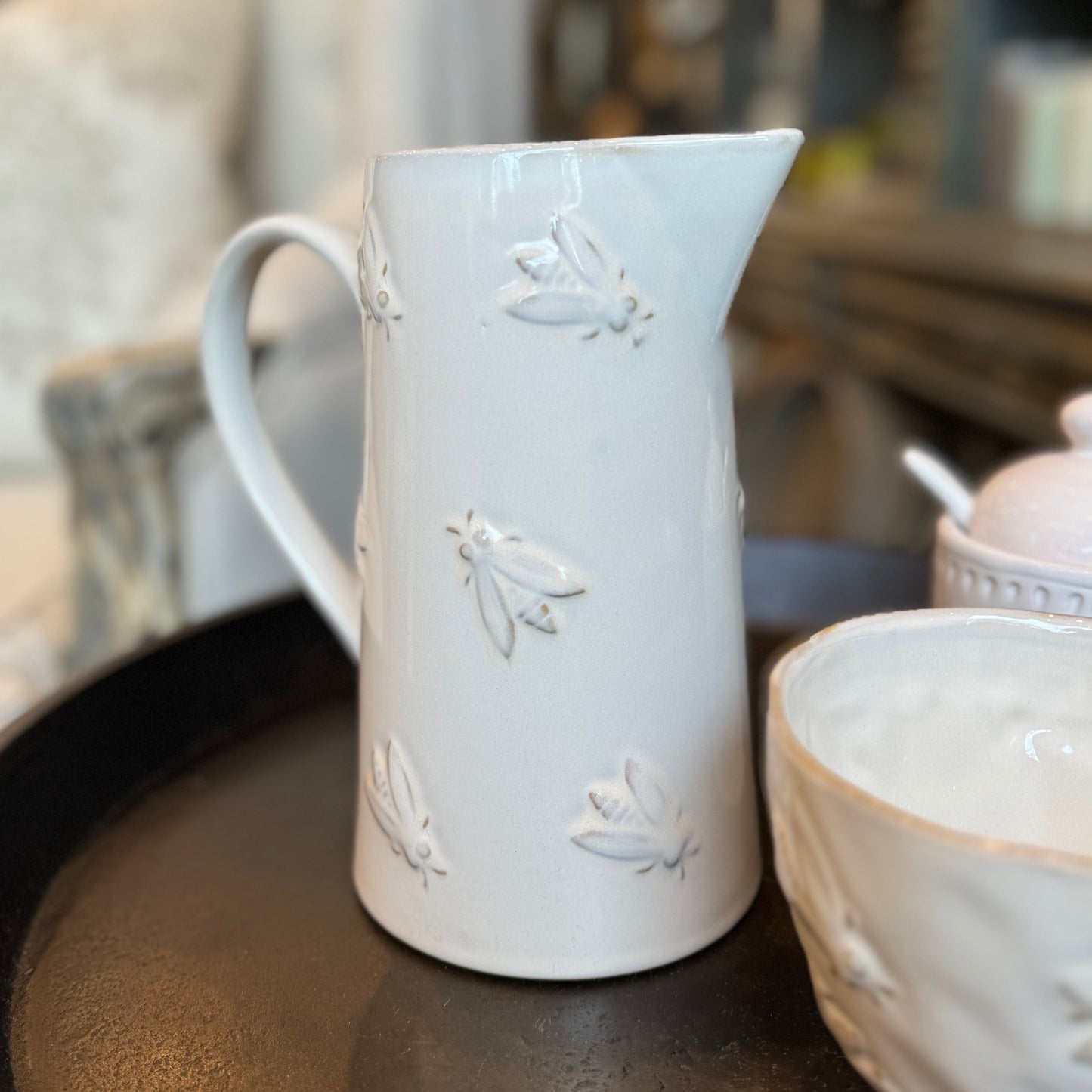 Experience the exquisite design of the Abeille Bee Cream Ceramic Jug, with an embossed bumblebee design and glossy cream-colored glaze. Perfect for holding water or displaying beautiful flowers, this jug adds a touch of elegance to any kitchen. Plus, its large, comfortable handle makes it easy to use. front