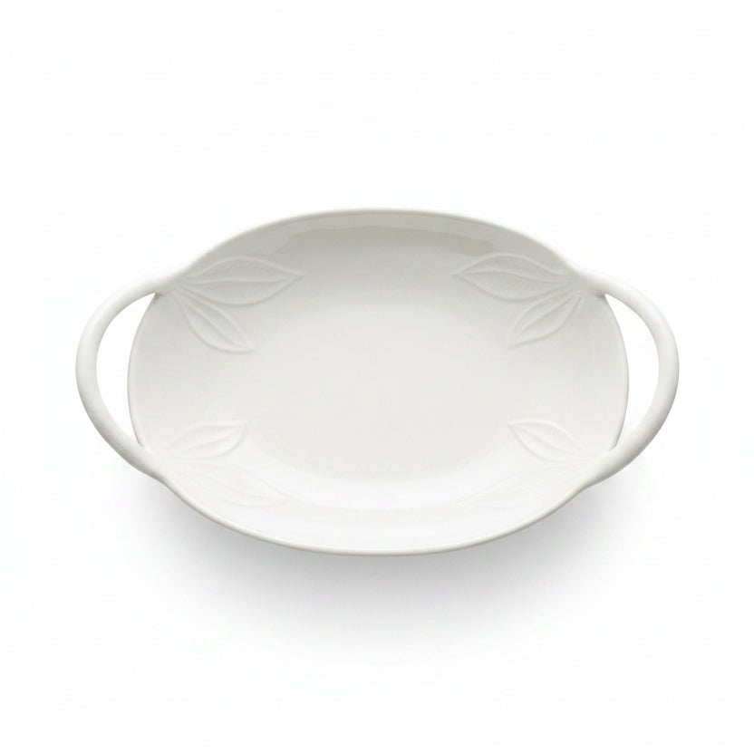 An oval white ceramic serving dish with two side handles and embossed leaf details,