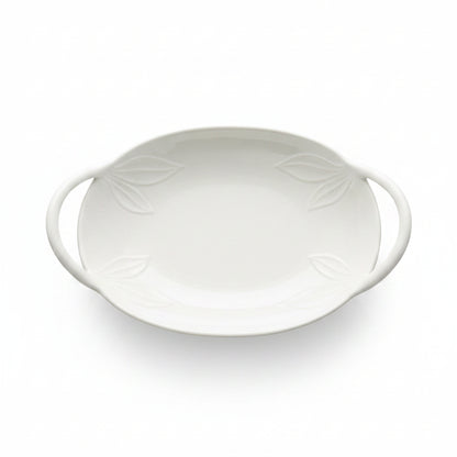 An oval white ceramic serving dish with two side handles and embossed leaf details,