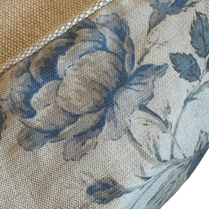 Close-up of a textured beige cushion with a blue floral print and a braided edge trim, resting on a matching beige upholstered surface.