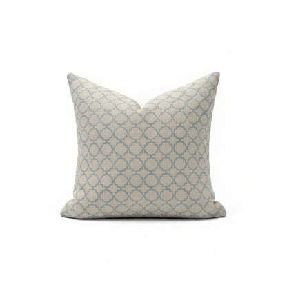 A square throw pillow with a blue and beige geometric trellis pattern, resting on a light beige upholstered armchair.