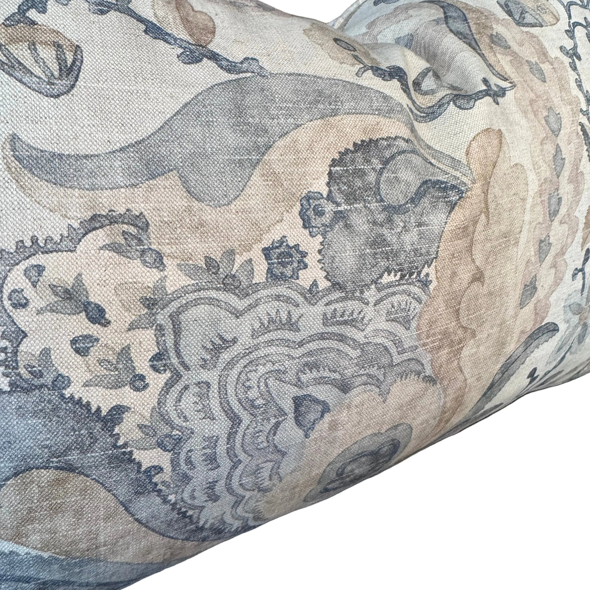A close-up of a decorative throw pillow featuring an intricate botanical and scroll pattern in muted blue-gray and beige tones on a textured fabric, set against a dark background.