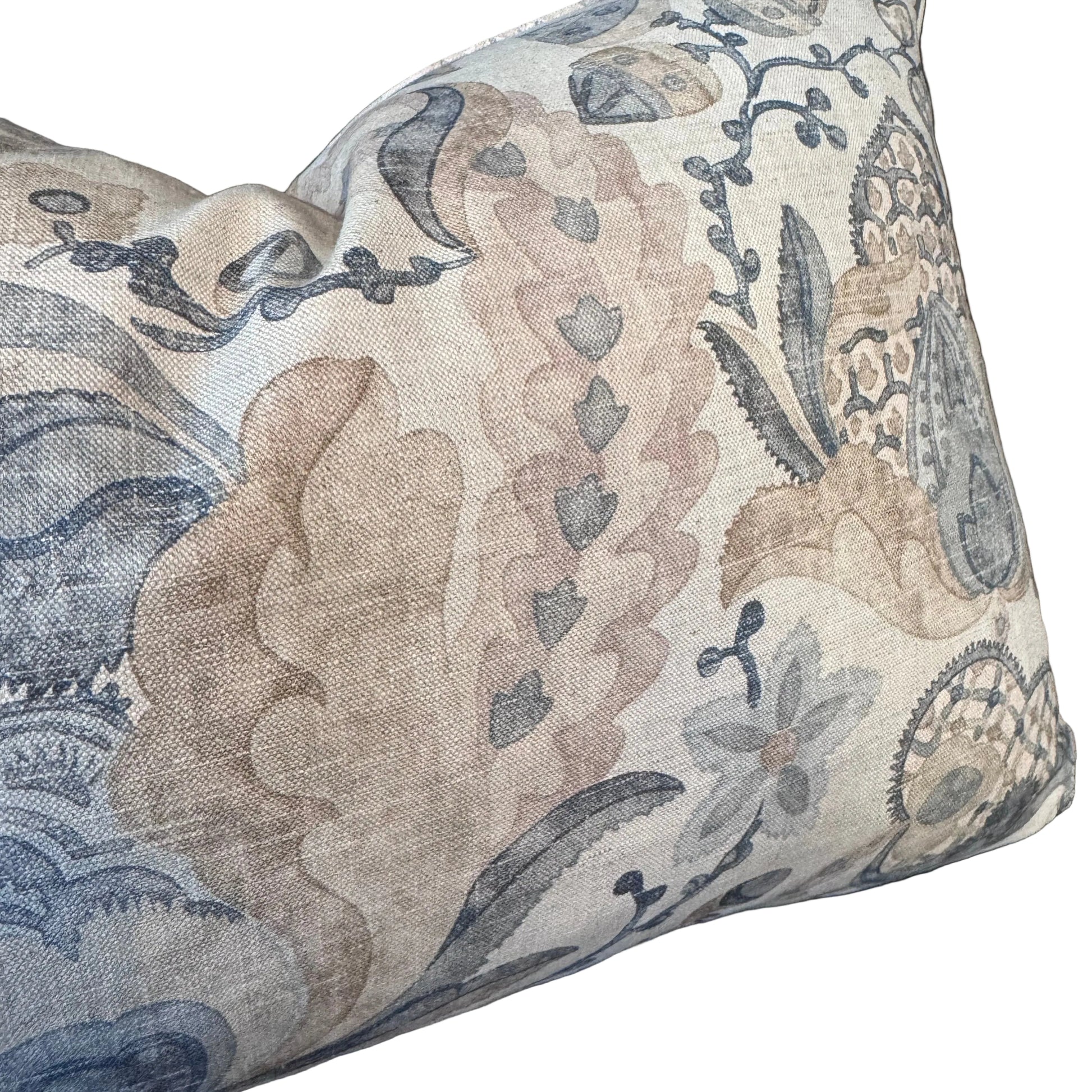 A square decorative throw pillow with a detailed botanical and floral pattern in muted beige, dusty pink, and slate blue on a textured linen-like fabric, resting on a dark background.