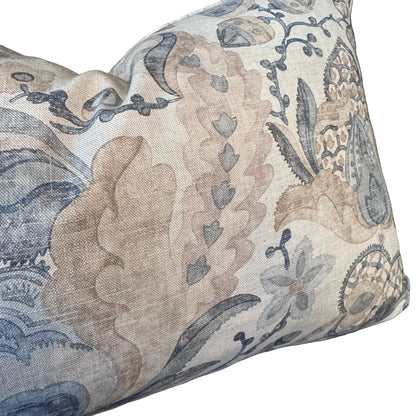 A square decorative throw pillow with a detailed botanical and floral pattern in muted beige, dusty pink, and slate blue on a textured linen-like fabric, resting on a dark background.