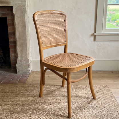 Wooden chair with wicker back and seat in a room with a fireplace and window.
