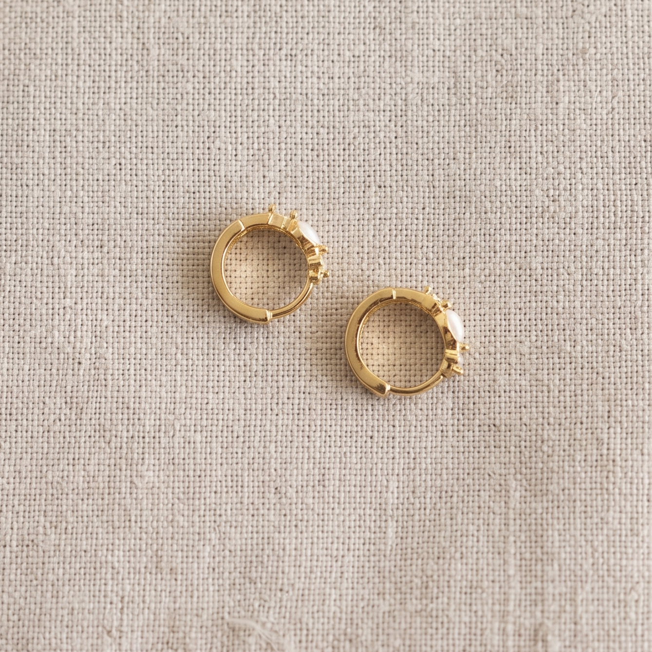 Pair of gold hoop earrings on a beige fabric background