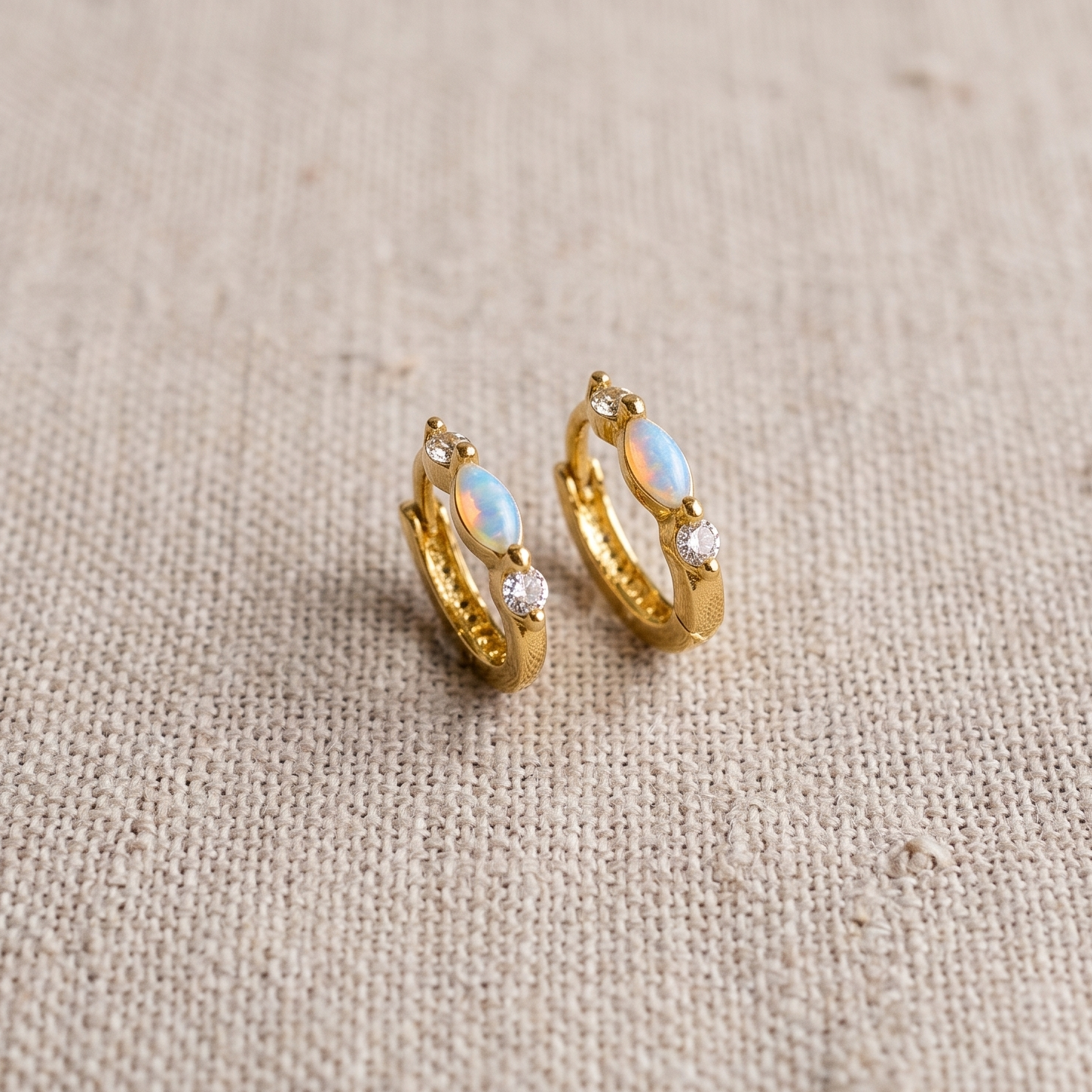 Gold hoop earrings with opal stones on a beige fabric background