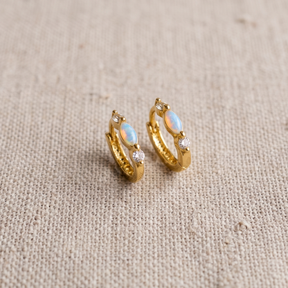 Gold hoop earrings with opal stones on a beige fabric background