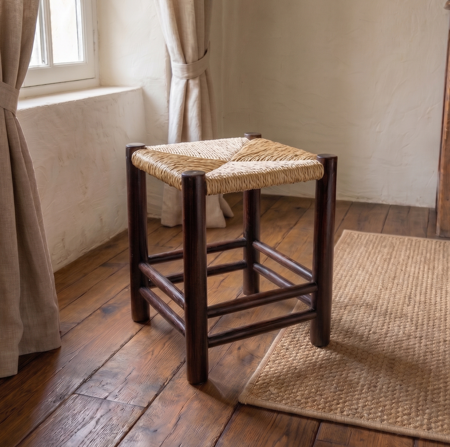 Wooden stool with woven seat on a wooden floor in a room with curtains and a rug.