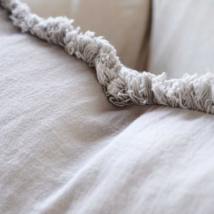 Indulge in the ultimate comfort with the Avery Linen Silver Grey Lumbar Cushion, made with 100% European Linen and adorned with a soft cotton fringe. The plump feather insert adds a touch of luxury, making it the most comfortable option available. Close up.