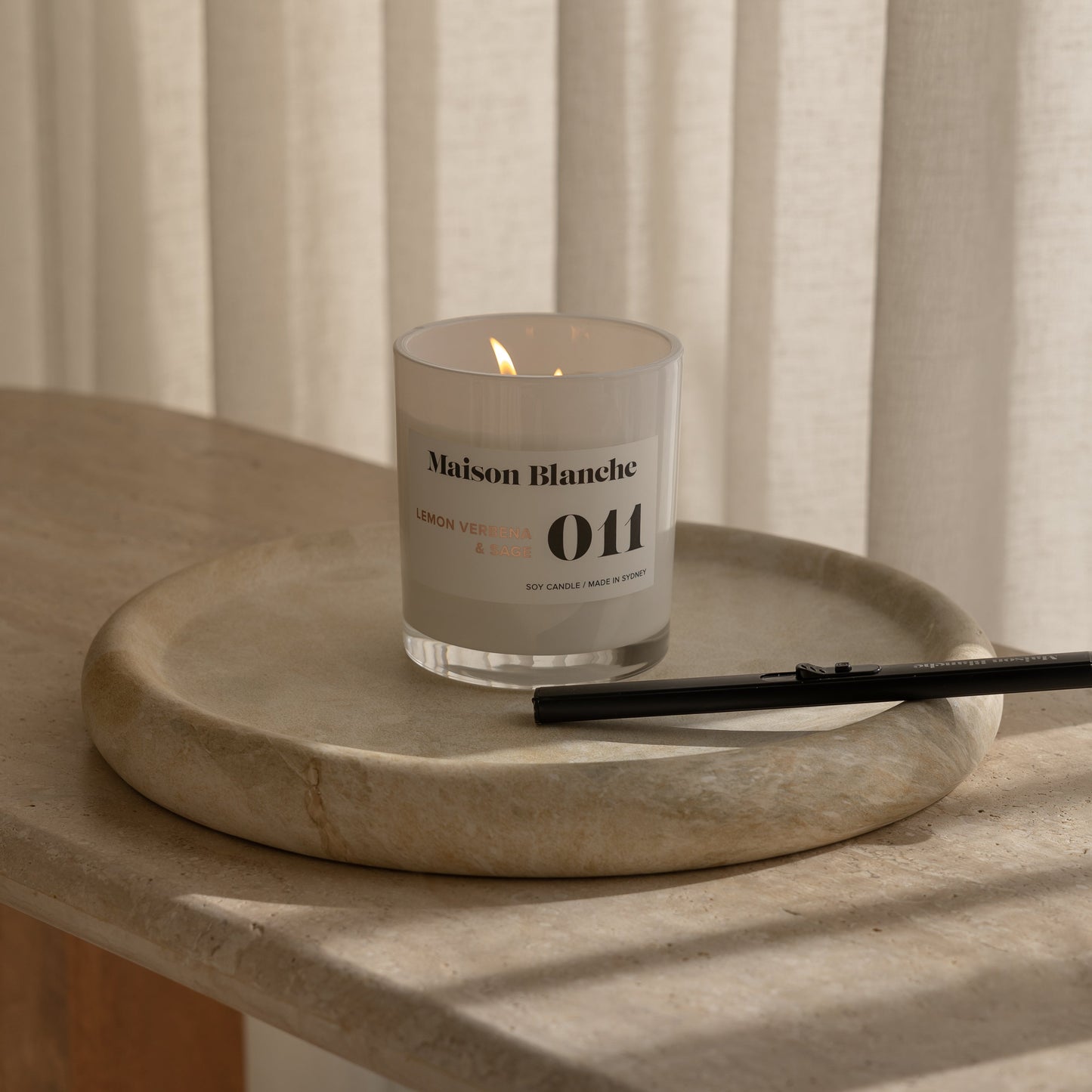Candle with a label on a stone surface in front of striped curtains