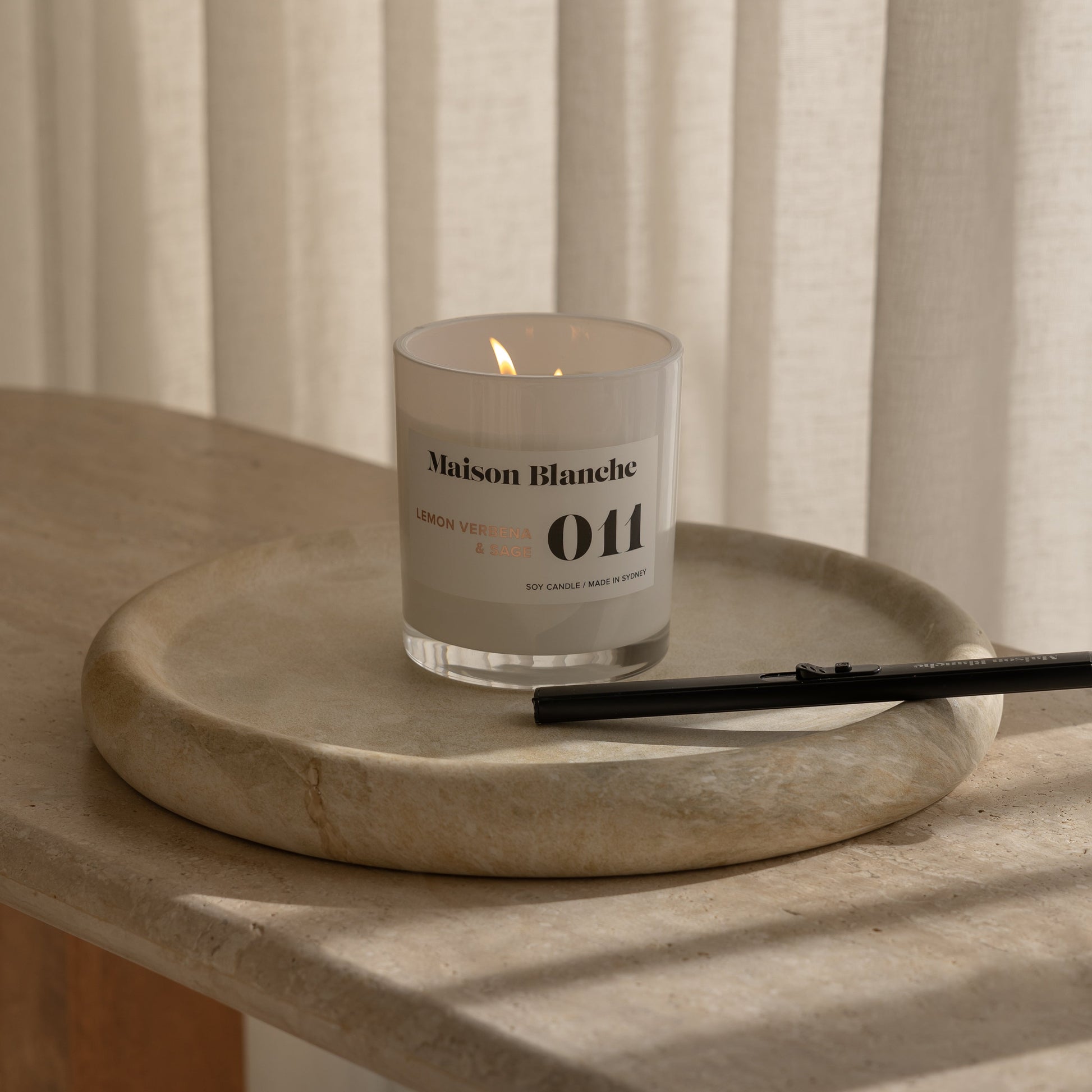 Candle with a label on a stone surface in front of striped curtains