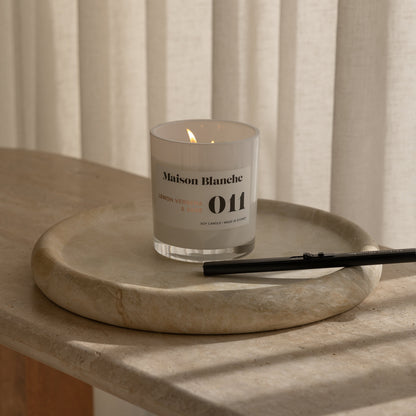 Candle with a label on a stone surface in front of striped curtains