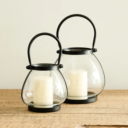 Two glass lanterns with black holders on a wooden surface.