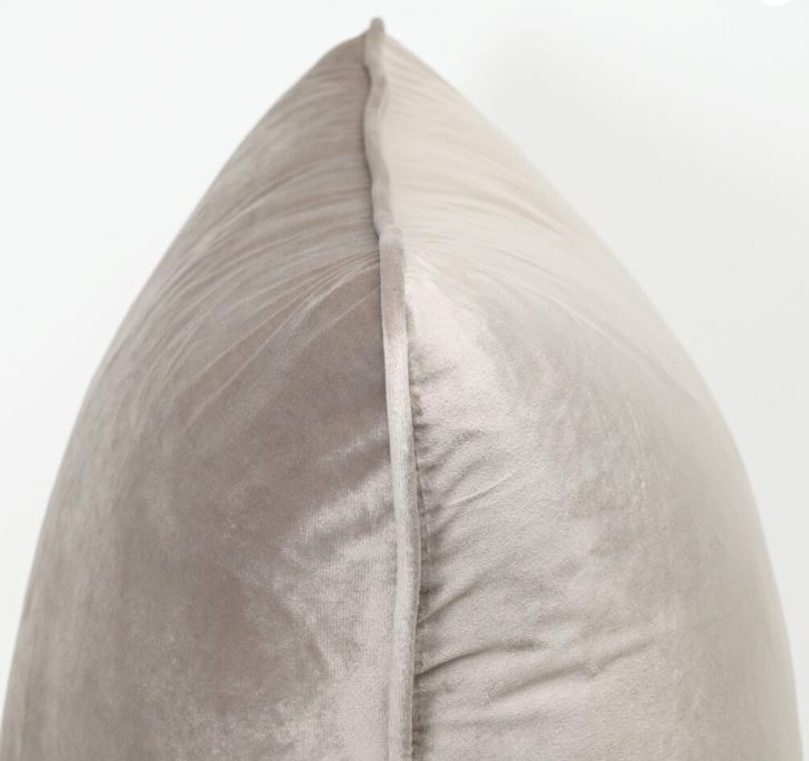 A close-up of a plush velvet throw pillow in a light taupe-gray color, showing the soft texture and a central seam against a plain white background.