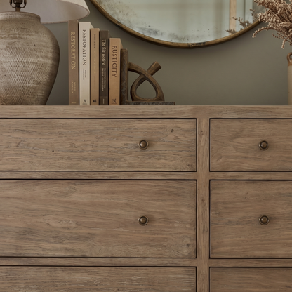 Wooden dresser with books, a lamp, and decorative items on top against a neutral wall.