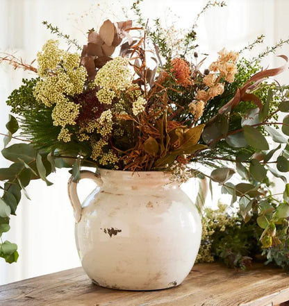 This exquisite aged white urn is expertly handcrafted from terracotta, providing a timeless vintage charm to any shelf or home decor. Its charming handle adds a sculptural touch and it is perfect for displaying fresh or faux flowers. Whether styled alone or with foliage, this terracotta piece brings warmth and style to any setting. Styled.