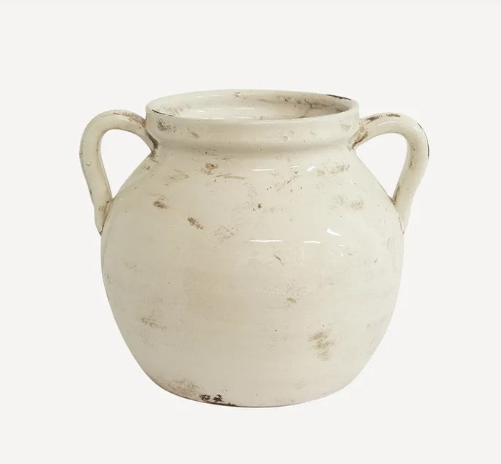 This exquisite aged white urn is expertly handcrafted from terracotta, providing a timeless vintage charm to any shelf or home decor. Its charming handle adds a sculptural touch and it is perfect for displaying fresh or faux flowers. Whether styled alone or with foliage, this terracotta piece brings warmth and style to any setting.