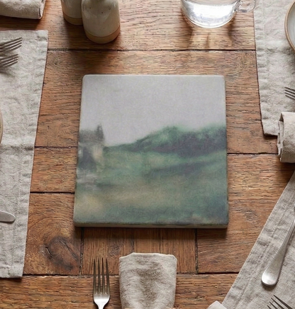 Dining table set with hand painted trivet silverware, and water pitcher on a wooden surface.