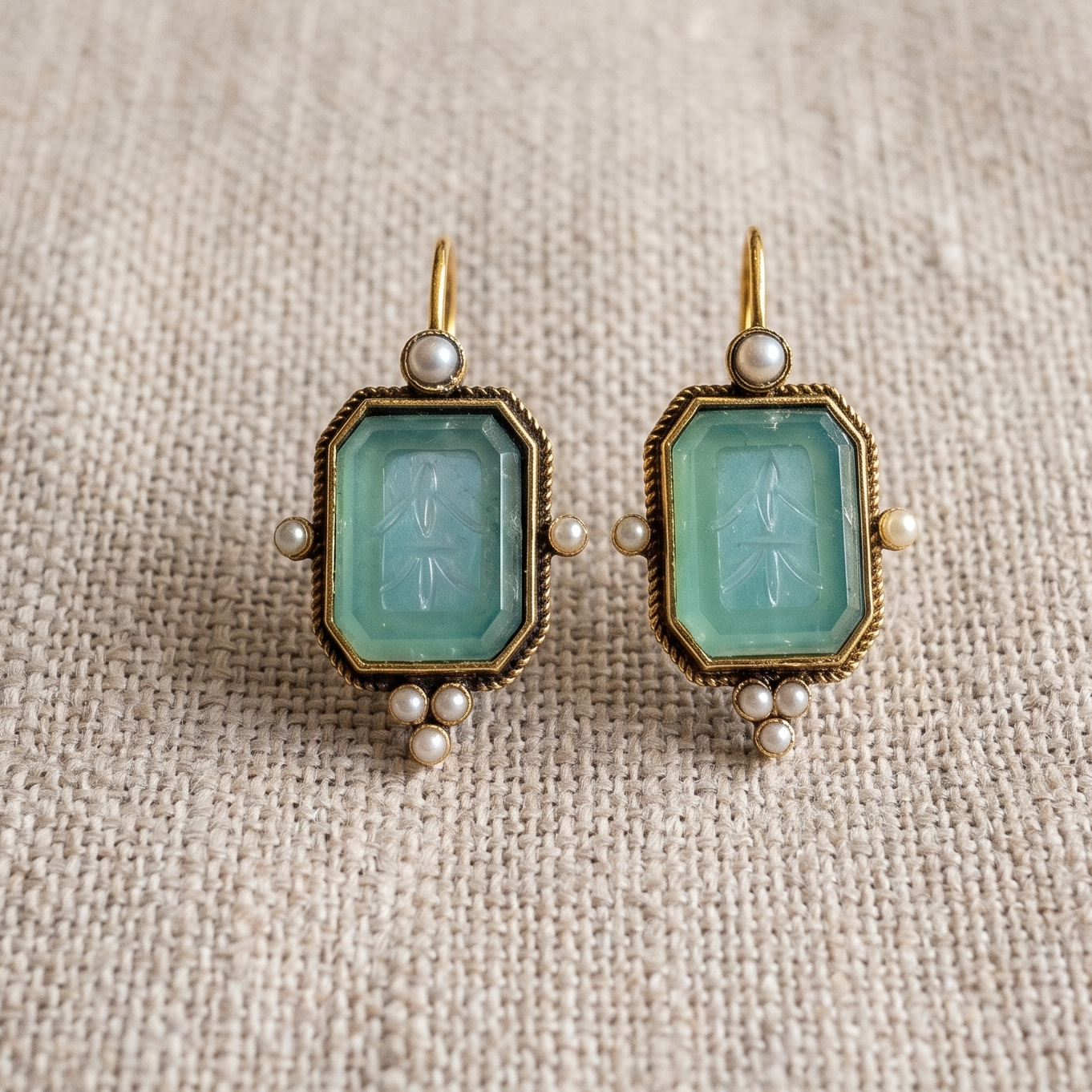 Pair of earrings with green gemstones on a textured beige fabric background