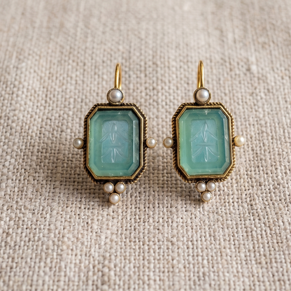 Pair of earrings with green gemstones on a textured beige fabric background