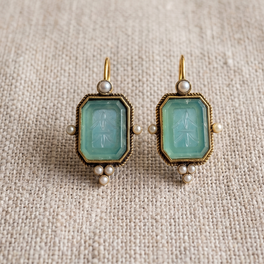 Pair of earrings with green gemstones on a textured beige fabric background