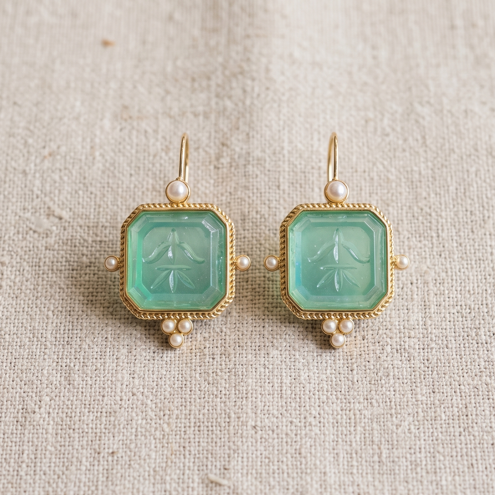 Pair of earrings with pale blue gemstones and gold accents on a beige fabric background