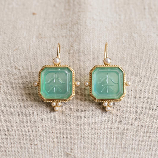Pair of earrings with pale blue gemstones and gold accents on a beige fabric background