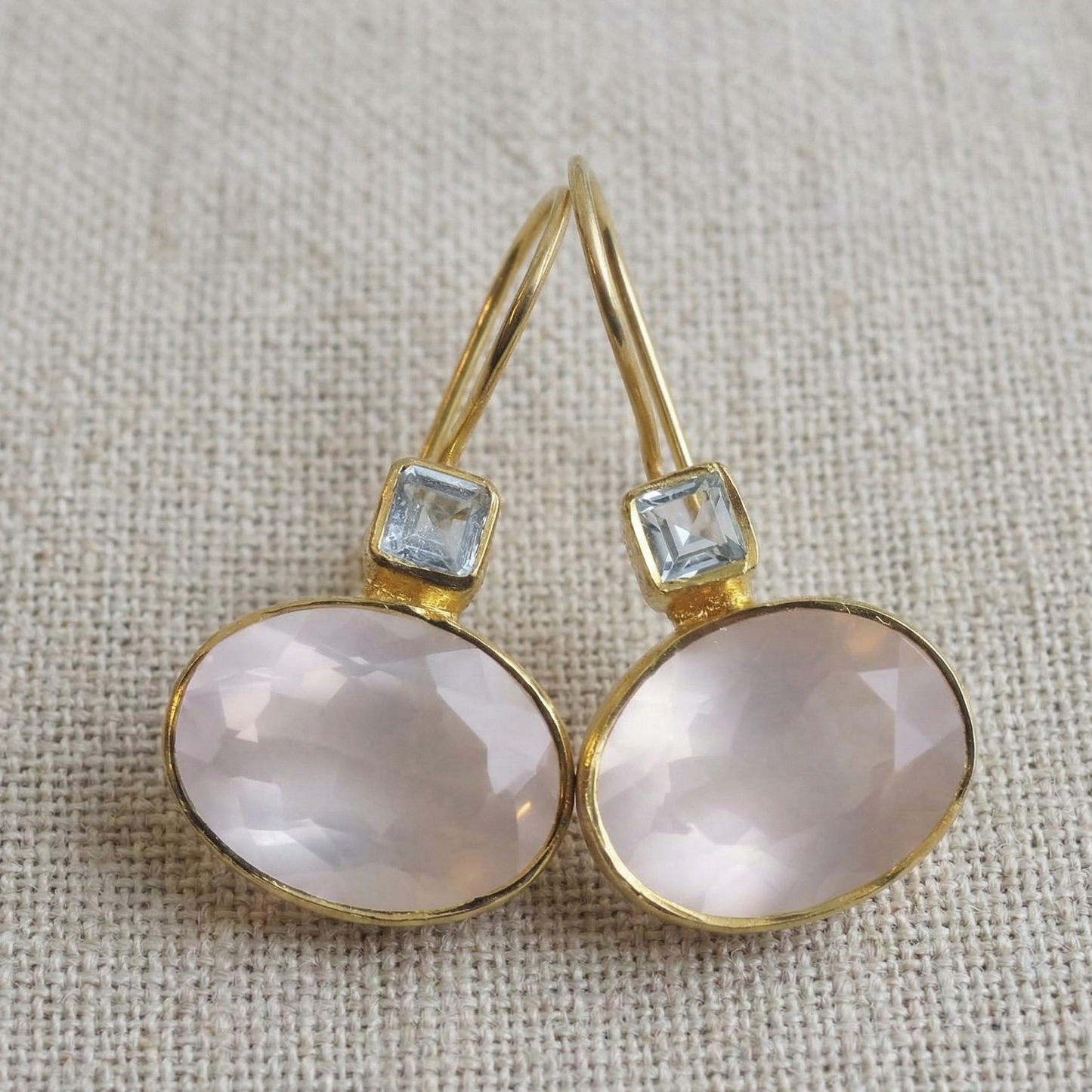 Gold earrings with pink stones and small blue stones on a textured beige background