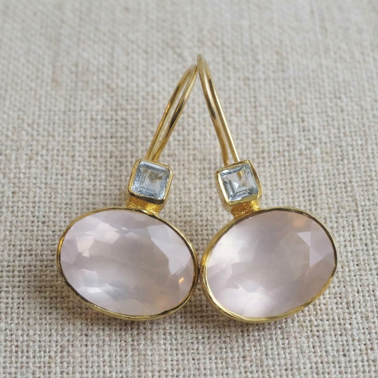 Gold earrings with pink stones and small blue stones on a textured beige background