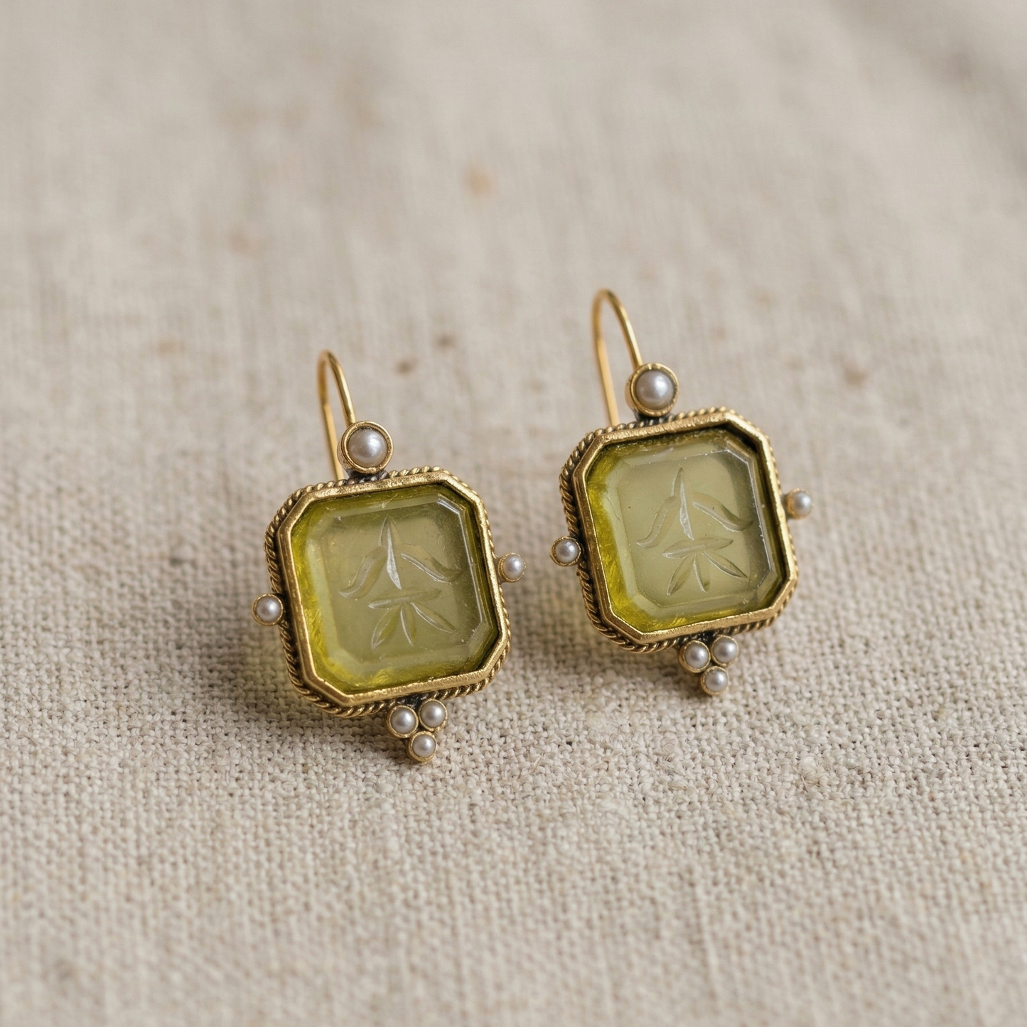 Pair of vintage-style earrings with green stone and gold frame on a textured beige background