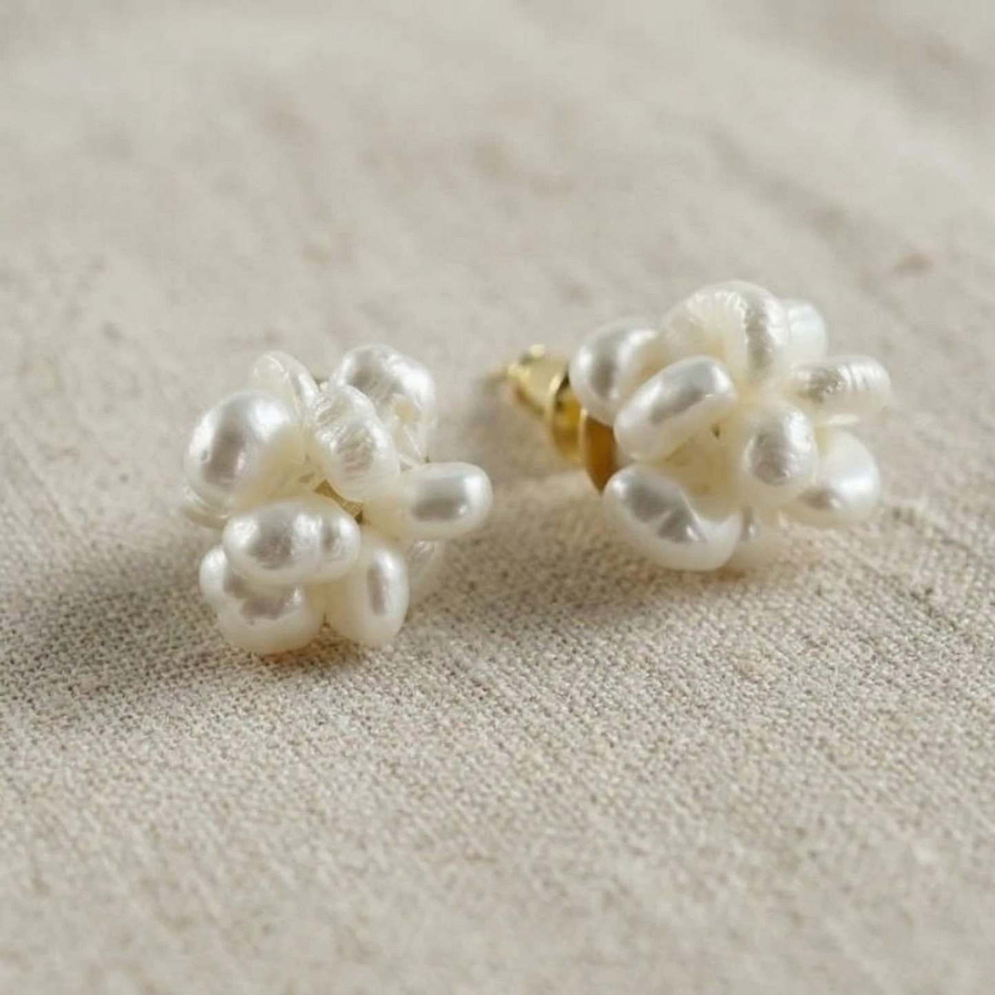 Pair of pearl earrings on a textured beige surface