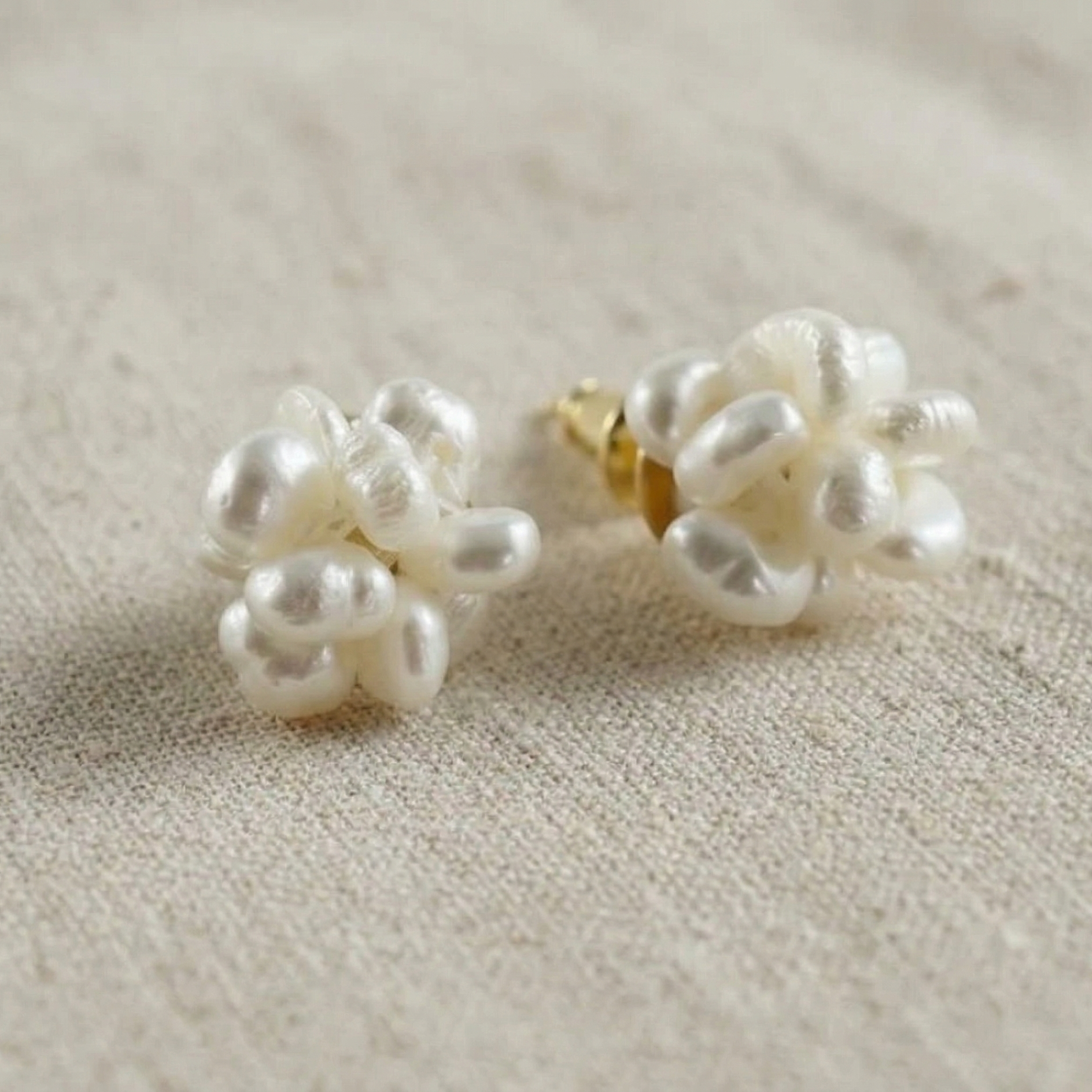 Pair of pearl earrings on a textured beige surface