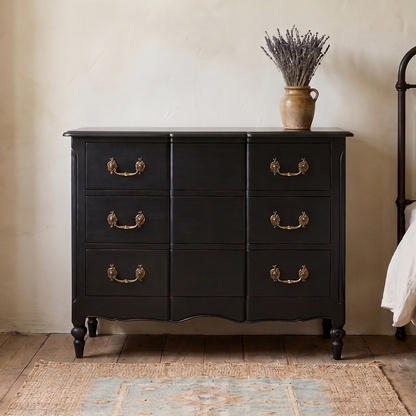 Black dresser with gold handles in a bedroom setting with a bed and decor.