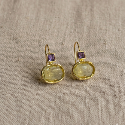 Gold earrings with gemstones on a textured beige fabric background