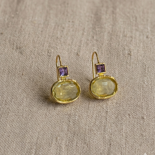 Gold earrings with gemstones on a textured beige fabric background