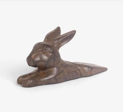 A small sculptural rabbit figurine in a metallic bronze finish, shown from the side against a plain light gray background.
