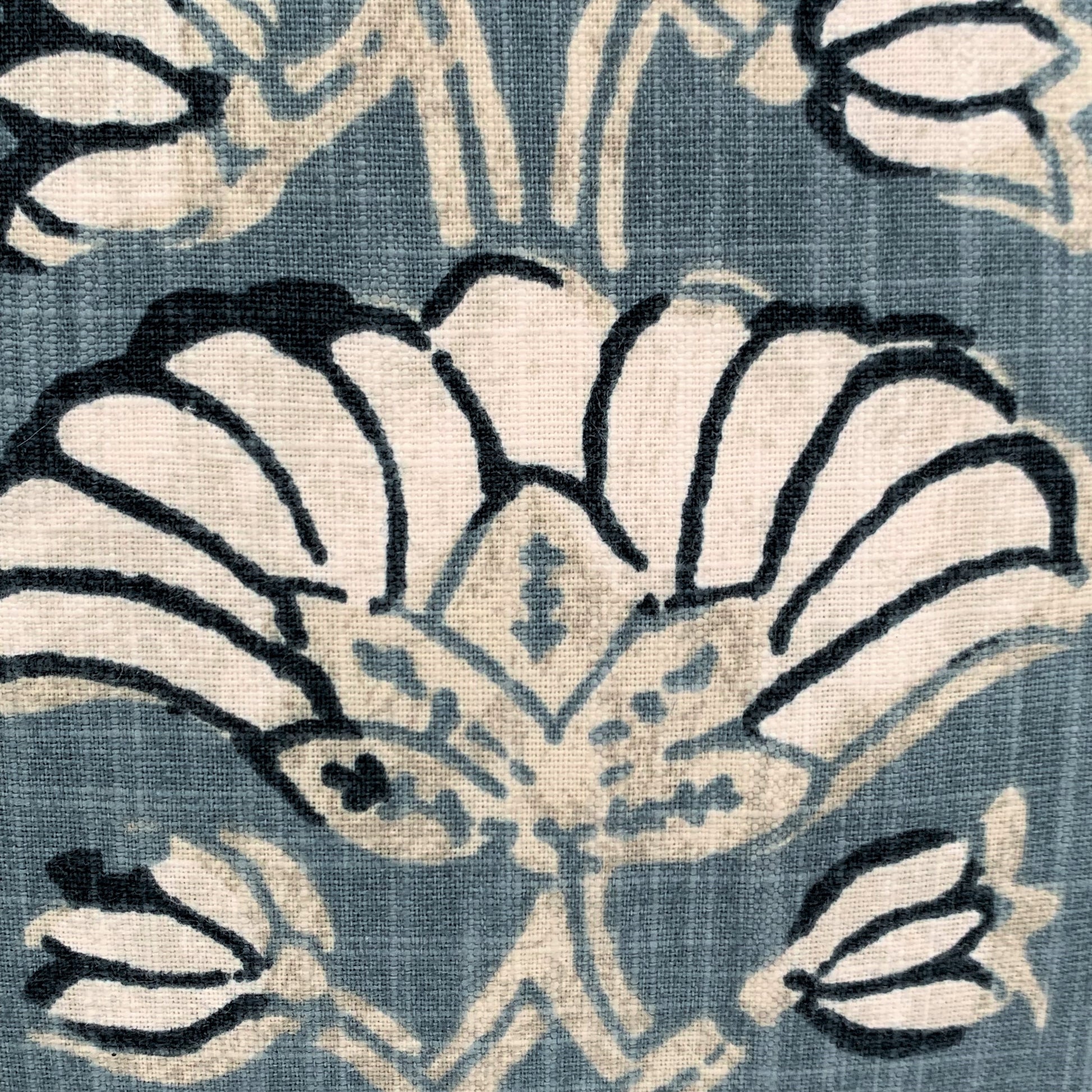 The heavyweight Pradesh Art Deco Floral Blue Taupe Cushion, featuring a refined pattern from Robert Allen Fabrics, is sure to add a touch of sophistication to any room. Utilizing a composition of pale taupe, off white, and blue hues, its feather-filled insert provides unparalleled comfort for a truly cozy feel. Close up detail.