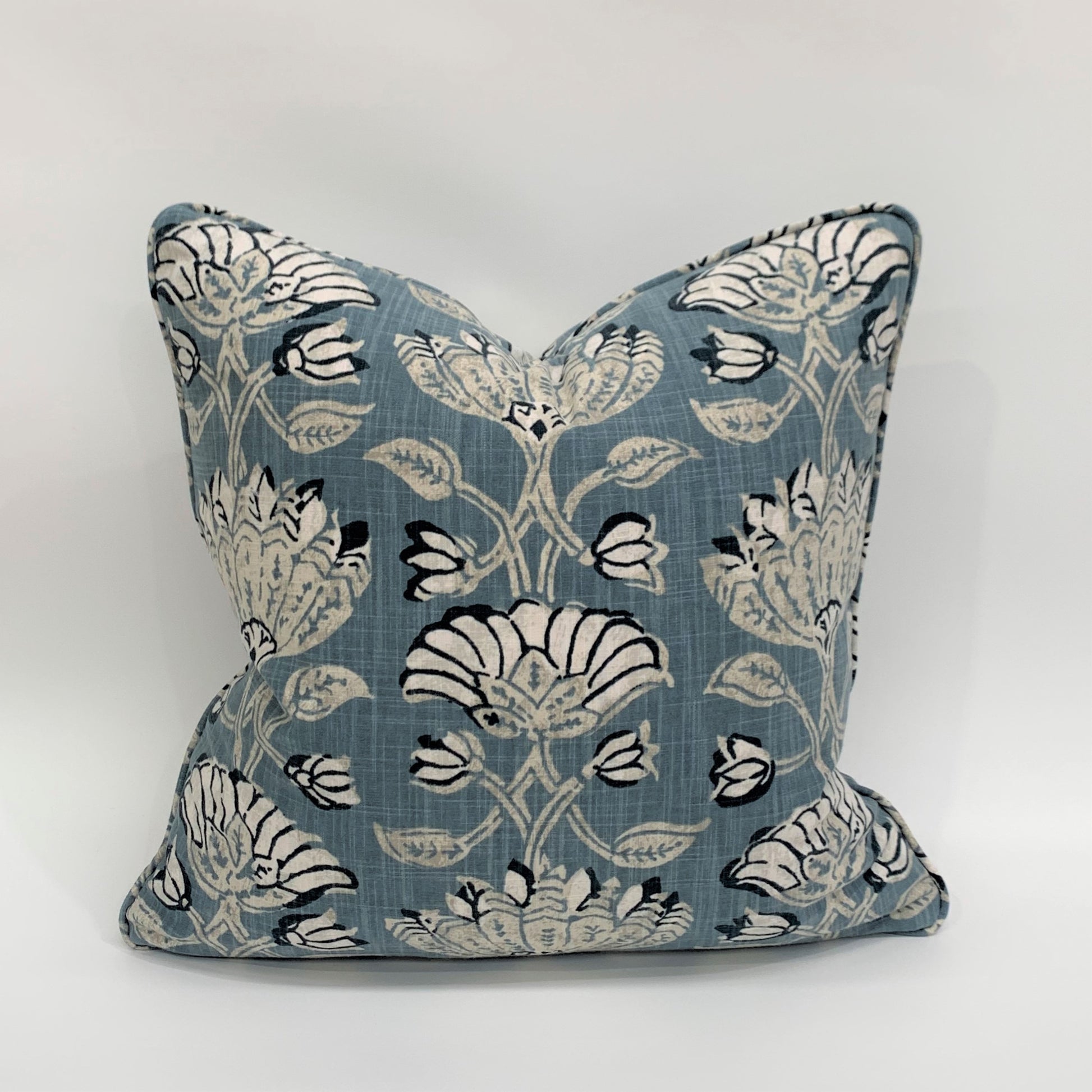 The heavyweight Pradesh Art Deco Floral Blue Taupe Cushion, featuring a refined pattern from Robert Allen Fabrics, is sure to add a touch of sophistication to any room. Utilizing a composition of pale taupe, off white, and blue hues, its feather-filled insert provides unparalleled comfort for a truly cozy feel. Front.