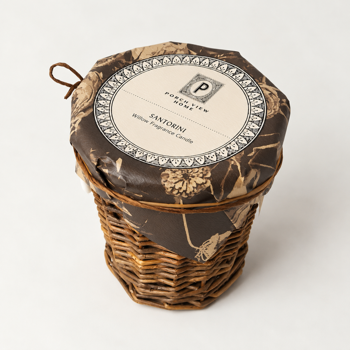 A wicker basket candle with a brown camouflage-patterned fabric liner and a round cream label that reads 'Punch Line Candle' and 'Santorini Willow Fragrance Candle,' photographed on a light gray background.