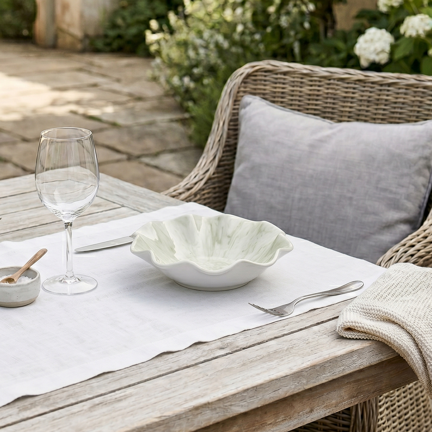 Outdoor dining setup with a wooden table, wicker chair, and garden view.