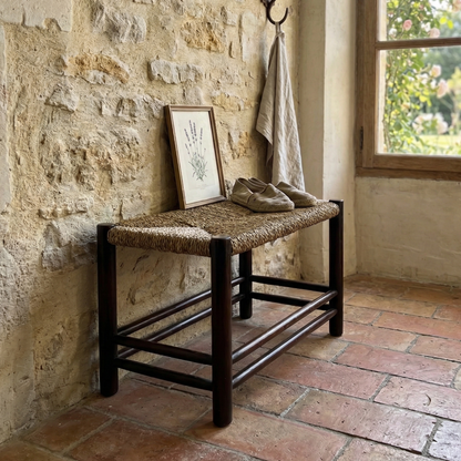 Woven bench against a stone wall with a framed picture and coat in a rustic room.