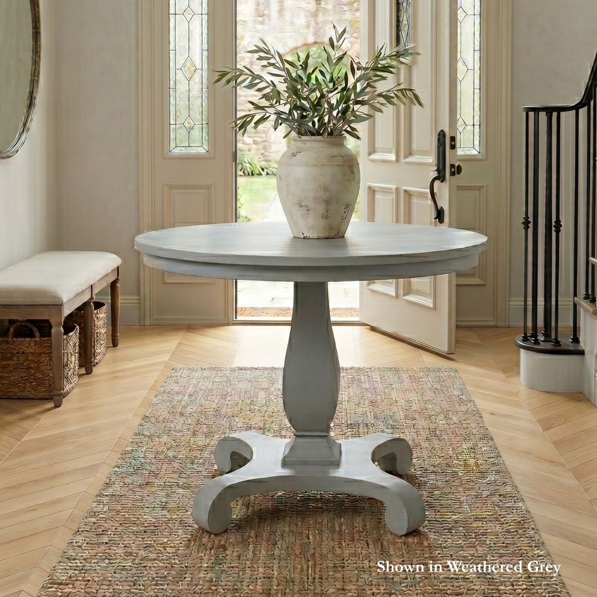 Round table with a vase of plants in a room with a door and bench.